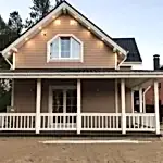 Toprak zemin üzerine konulmuş arkası ağaçlık bol pencereli ahşap ev ön görseli