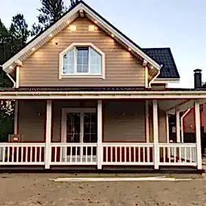 Toprak zemin üzerine konulmuş arkası ağaçlık bol pencereli ahşap ev ön görseli