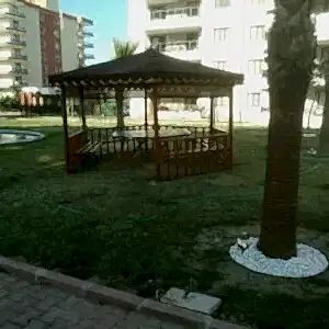 Palmiye ağaçları arasında yerleri çim olan bahçede konumlandırılmış altıgen kamelya görseli