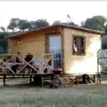 Ağaçlar içinde mangal ve verandasında oturan üç bayanı olan ahşap karavan