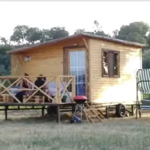 Ağaçlar içinde mangal ve verandasında oturan üç bayanı olan ahşap karavan