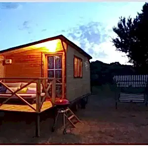 Hafif güneş batarken çekilmiş verandasının ışığı yanan ahşap karavan modelleri görseli