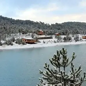 Karlarla kaplı orman ve göl manzarası arasında ahşap kafe restaurant tesisi