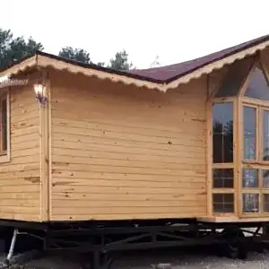 Adanın üzerinde yerler toprak zemin ve arkası ağaçlık alanda konumlanmış önü camekan ve giriş bölümü korunaklı 2+1 Tiny House fiyatları görseli